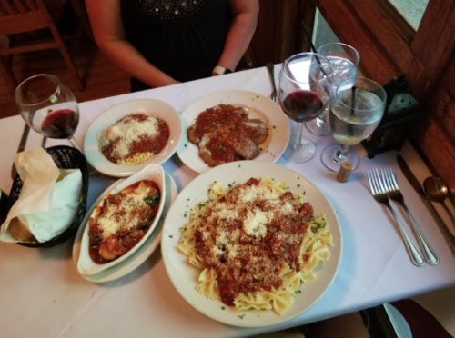 A table set with three pasta dishes, red wine, and water glasses, with a person partially visible in the background.