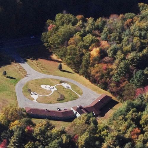 Aerial view of a circular driveway surrounding a building, with trees and autumn foliage in the background.