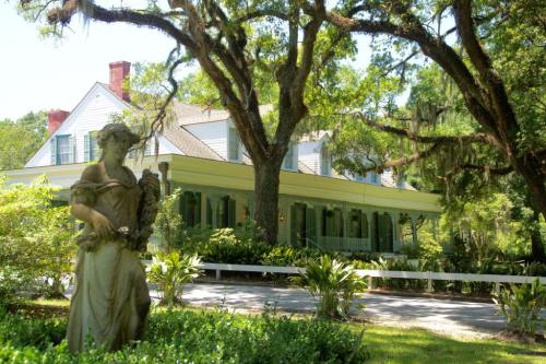 A historic house with green shutters, surrounded by trees and a statue in the foreground.