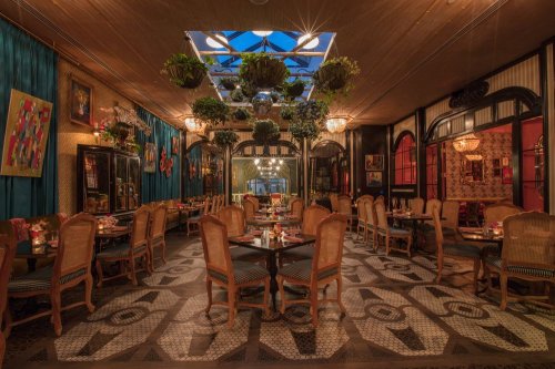 A stylish restaurant interior with wooden chairs, patterned flooring, and hanging plants, illuminated by soft lighting.