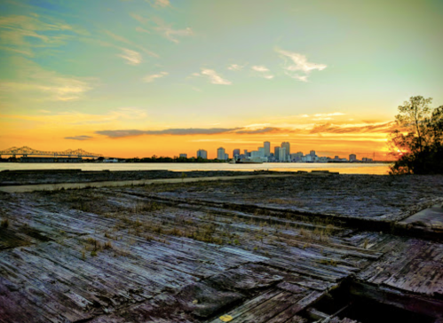 Sunset over a city skyline with a river in the foreground and wooden structures, creating a serene atmosphere.