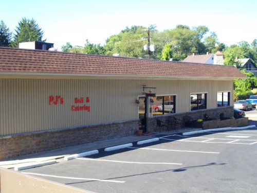 Exterior view of PJ's Deli & Catering, featuring a stone facade and large windows, with parking spaces in front.