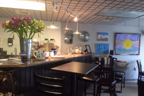 Cozy café interior with a counter, flowers, artwork on the walls, and tables for seating.