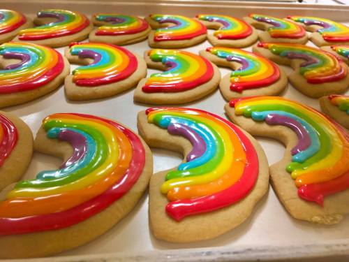 A tray of colorful rainbow-shaped cookies with vibrant icing in red, orange, yellow, green, blue, and purple.