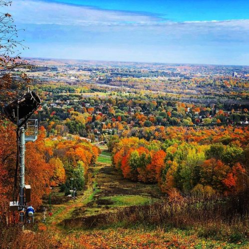 A scenic view of a valley filled with autumn foliage, featuring a ski lift and vibrant orange and yellow trees.