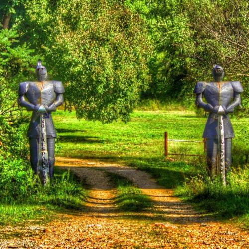 Two knight statues stand guard on either side of a grassy path, surrounded by trees and greenery.