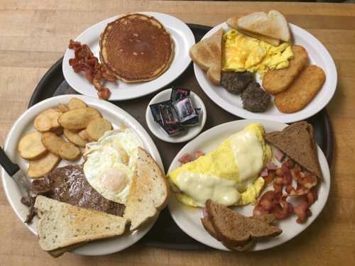 A tray with two plates: one with steak, eggs, toast, and potatoes; the other with pancakes, bacon, and an omelet.