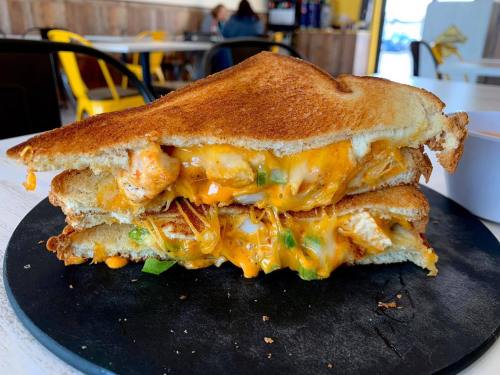 A stacked grilled cheese sandwich with melted cheese, chicken, and green peppers, served on a black plate.