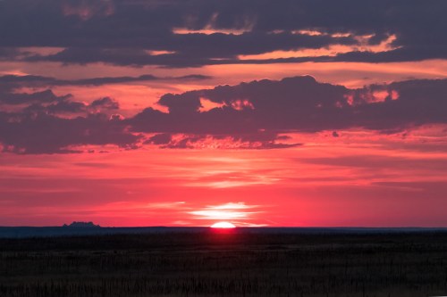 A vibrant sunset paints the sky in shades of pink and orange, with dark clouds scattered above a distant horizon.