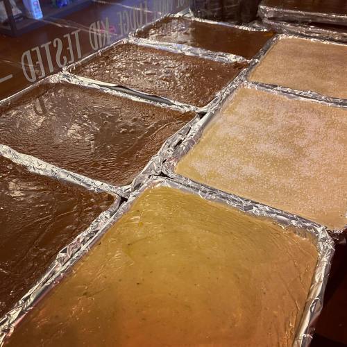 Trays of various batters or mixtures, some with a shiny surface, lined with foil and placed on a counter.