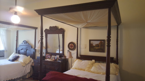 A cozy bedroom featuring a four-poster bed, dresser, mirror, and warm lighting.