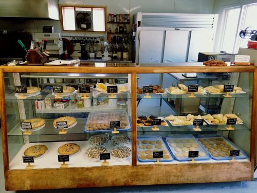 A bakery display case filled with various baked goods, including pies, cookies, and pastries, labeled with small signs.