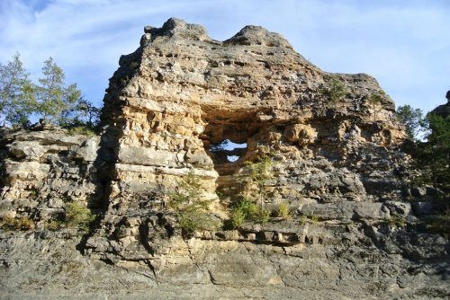 Rock formation with a large arch and greenery, set against a blue sky.