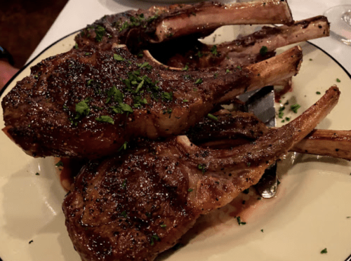 Three grilled lamb chops garnished with herbs, served on a plate with a rich sauce.