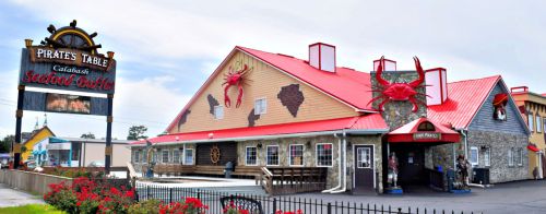 A seafood buffet restaurant with a red roof, crab decorations, and a sign reading "Pirate's Table" in a coastal setting.