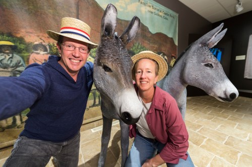 Two people in straw hats pose for a selfie with two donkey sculptures in an art exhibit.