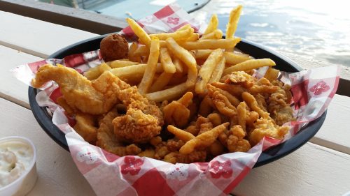 A basket of fried chicken pieces, French fries, and a hush puppy, served with a side of dipping sauce.