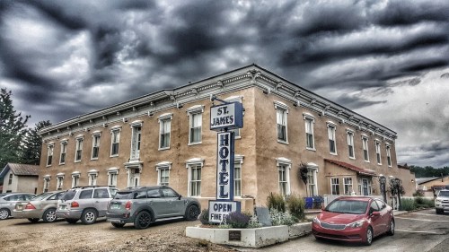 Historic St. James Hotel with a cloudy sky, featuring a sign that reads "Open" and parked cars in front.