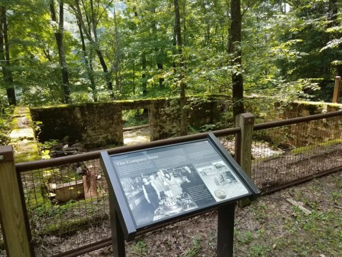 Ruins of a company store surrounded by trees, with an informational sign in the foreground.