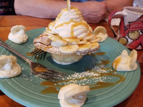 A dessert featuring a cupcake topped with whipped cream, banana slices, and caramel sauce, surrounded by dollops of whipped cream.