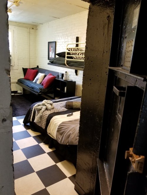 A small room with a bed, a futon, and a black-and-white checkered floor, viewed through a doorway.