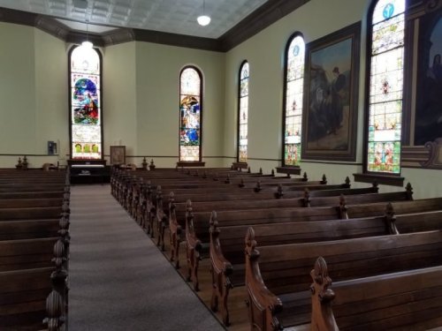 Interior of a church featuring wooden pews and colorful stained glass windows.