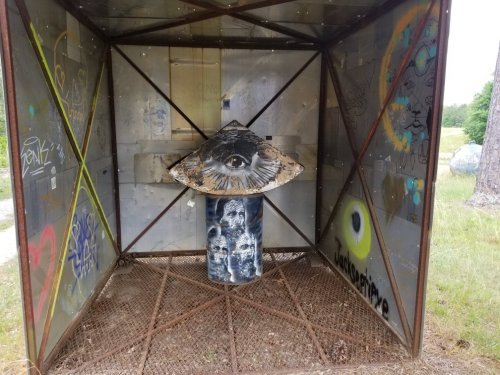 A metal structure with graffiti, featuring a painted eye on a cylindrical base in the center.