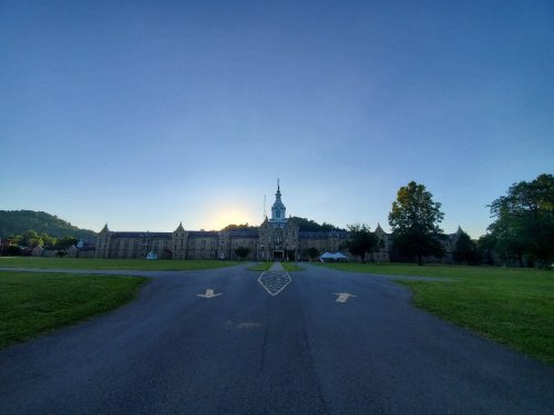 A historic building at sunrise, surrounded by green grass and trees, with a clear blue sky above.