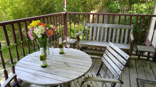 A cozy outdoor patio with a wooden table, chairs, a vase of flowers, and two glasses beside bottles.