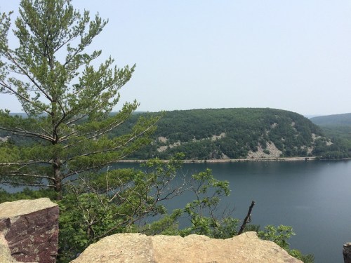 A serene view of a lake surrounded by green hills and trees under a clear sky.