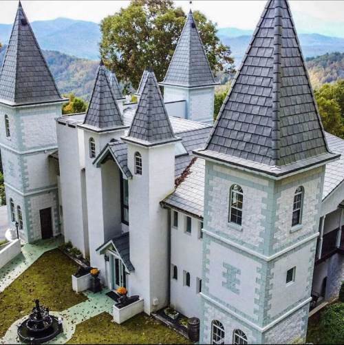 A whimsical castle with multiple spires, surrounded by greenery and mountains in the background.