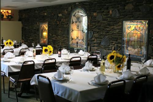 A dining room with tables set for a meal, featuring sunflower centerpieces and stained glass windows on a stone wall.