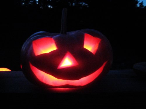 A carved pumpkin with a smiling face, glowing warmly from within against a dark background.