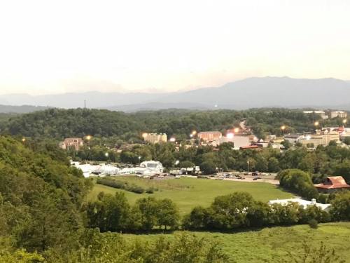 A scenic view of a small town surrounded by hills, with lights twinkling in the evening and mountains in the background.