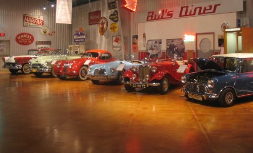 A vintage car display featuring several classic cars in a diner-themed setting with retro signage.