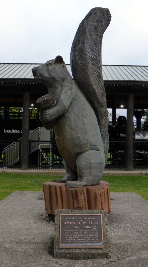 A wooden statue of a squirrel holding an acorn, with a plaque dedicated to Amos J. Peters.