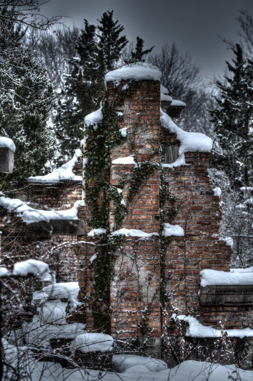 Snow-covered brick ruins with ivy, surrounded by leafless trees in a winter landscape.