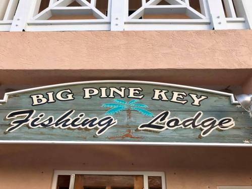Sign for "Big Pine Key Fishing Lodge" featuring a palm tree design, mounted on a textured wall.