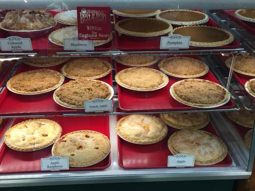A display case filled with various pies, including apple, blueberry, pumpkin, and Dutch apple, on red trays.