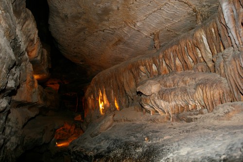 A dimly lit cave interior featuring unique rock formations and illuminated areas, showcasing natural textures and colors.