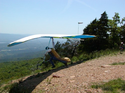 A person prepares to launch a hang glider from a rocky hillside, with a scenic view of mountains in the background.