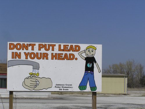 A colorful sign reads "Don't Put Lead in Your Head" with a cartoon character and a hand holding a rock.