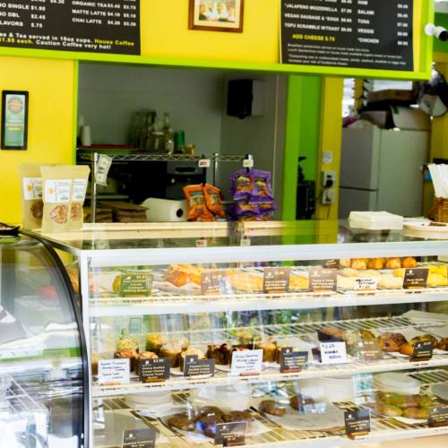 A colorful café display case filled with baked goods, with a menu board above and vibrant yellow walls.