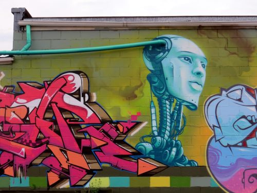 A colorful mural featuring a robotic head and vibrant graffiti letters on a wall.