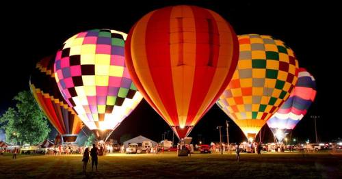 Colorful hot air balloons illuminated at night, surrounded by people and festival activities.