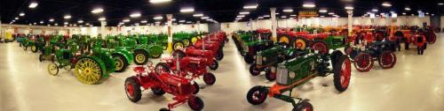 A panoramic view of a museum showcasing a variety of vintage tractors in vibrant colors, arranged in rows.