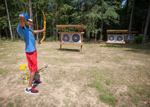 A person aiming a bow and arrow at target boards in a wooded archery range.