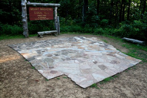 A stone platform at Mount Magazine's Signal Hill, surrounded by trees, with a wooden sign indicating the location.