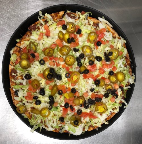 A large pizza topped with lettuce, tomatoes, black olives, and jalapeños on a metal surface.
