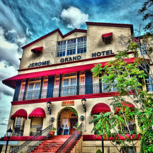 Historic Jerome Grand Hotel with red awnings and a blue sky, surrounded by greenery. A unique architectural landmark.